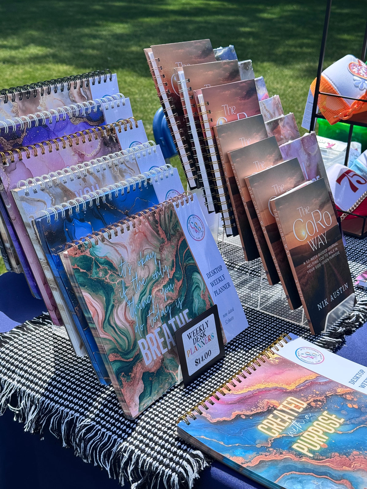 Stack of CoRo & Co. weekly desk planners with various designs on a vendor table.