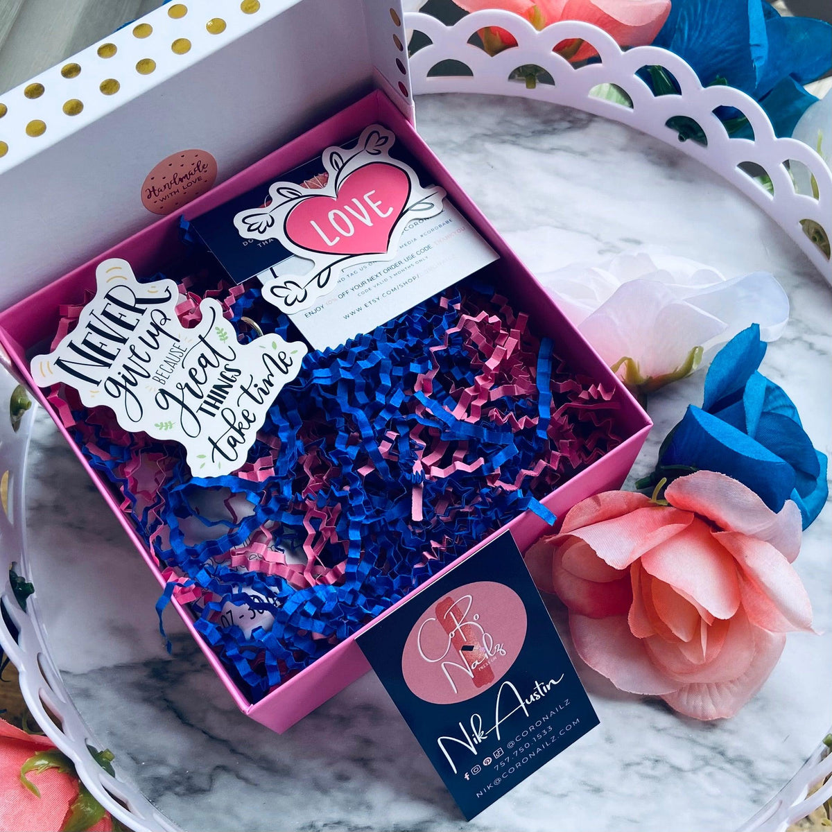 Gift box with decorative paper and a card on a marble surface with flowers.