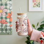 Hand holding a tumbler with cartoon ghost designs against a floral and checkered background