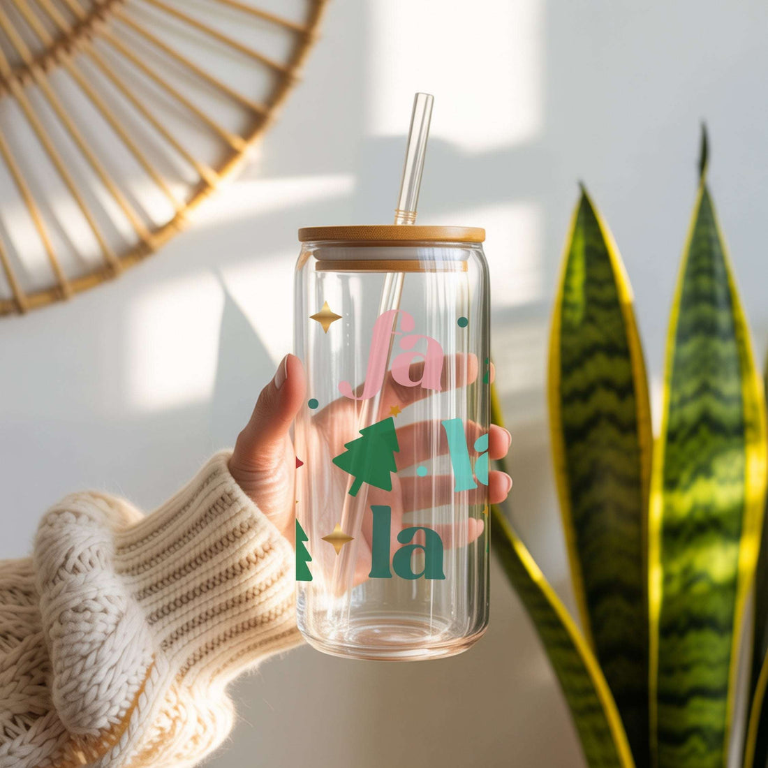 Glass tumbler with wooden lid and straw held by a person, with decorative elements on a light background.