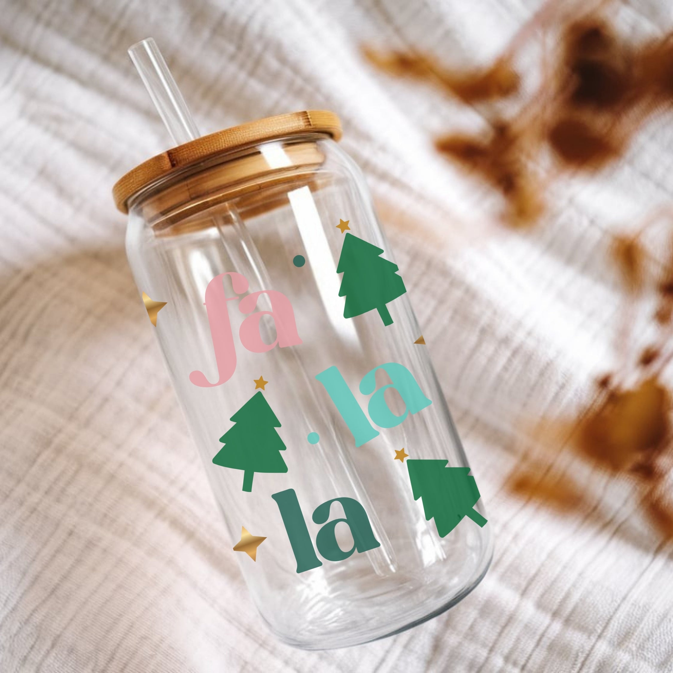 Clear tumbler with 'fa la la' and Christmas tree designs on a textured surface