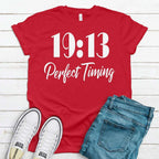 Red t-shirt with '19:13 Perfect Timing' text, white sneakers, and blue jeans on a wooden surface.