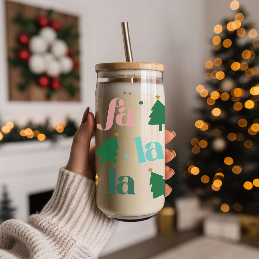 Hand holding a Christmas-themed tumbler with 'fa la la' text and tree designs against a festive background.