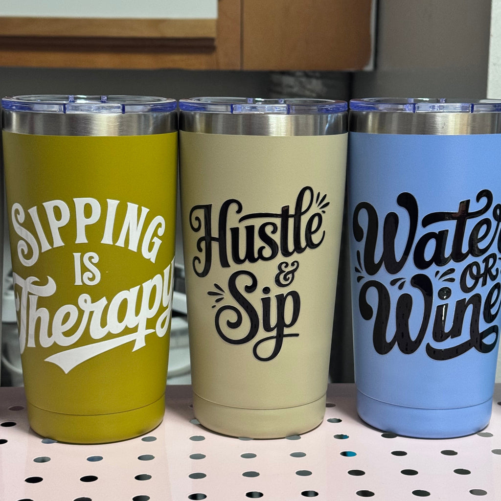 Three 20oz tumblers with motivational phrases on a pegboard.