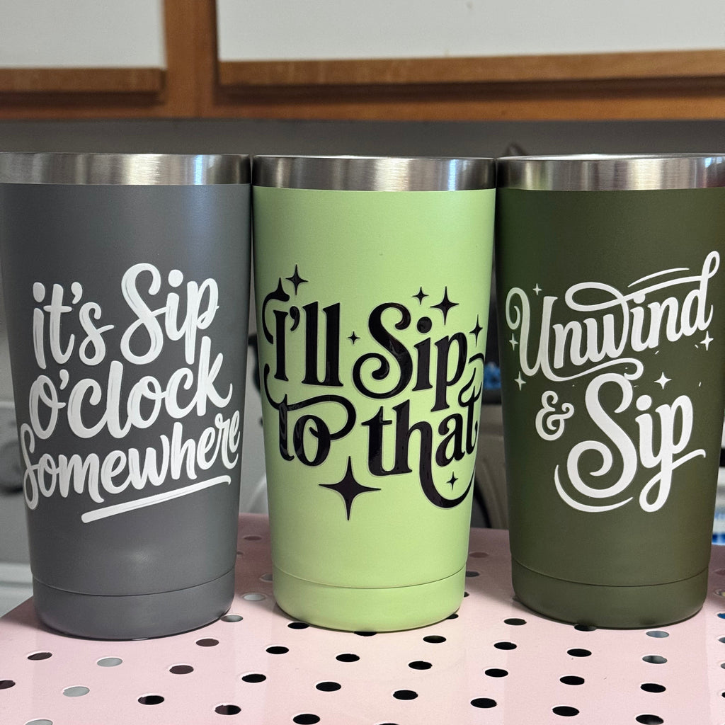 Three insulated tumblers with humorous text designs on a pegboard.