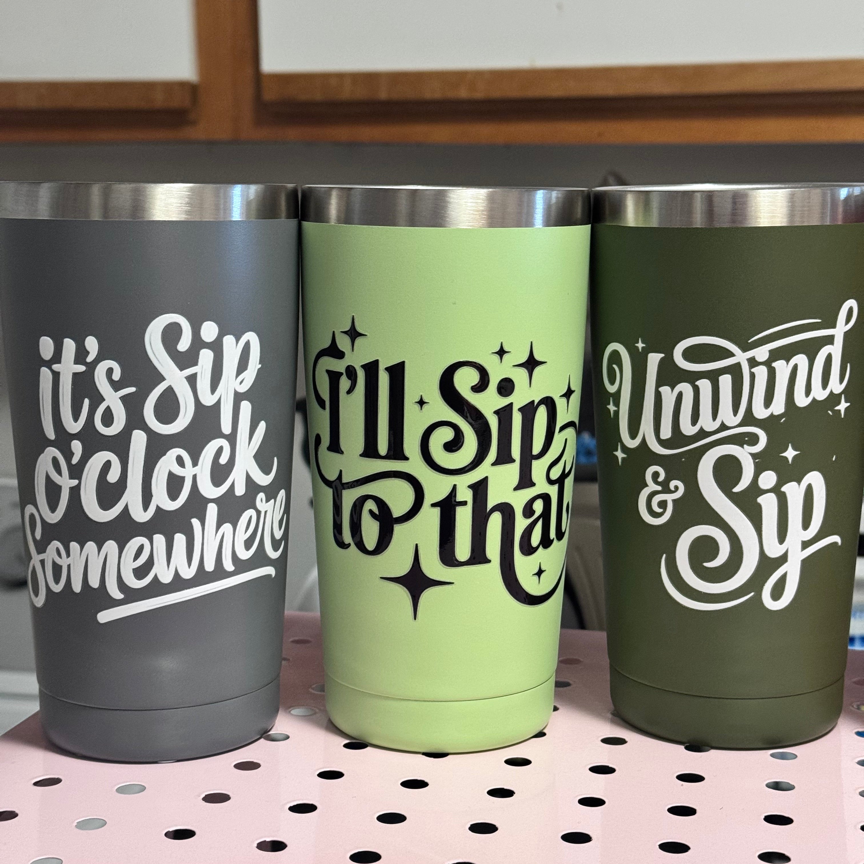 Three insulated tumblers with humorous text designs on a pegboard.