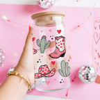 Glass jar with cowboy boot and cactus design held by a hand on a pink background