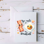Card with cartoon bacon and egg design on a wooden surface