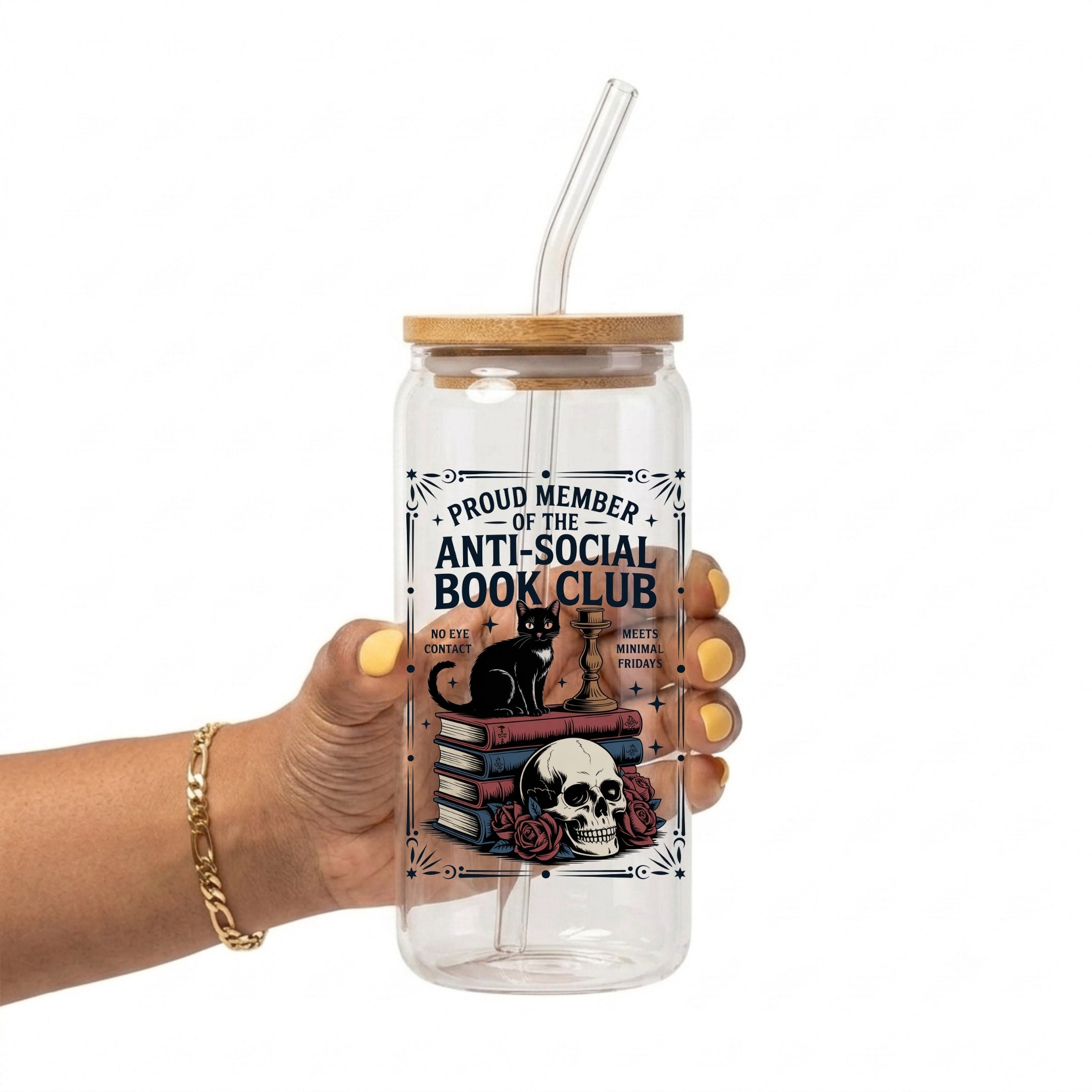 A hand holding a clear glass tumbler with a bamboo lid and clear straw. The tumbler features a graphic design with a black cat on books and a skull, with the text 'PROUD MEMBER OF THE ANTI-SOCIAL BOOK CLUB'.