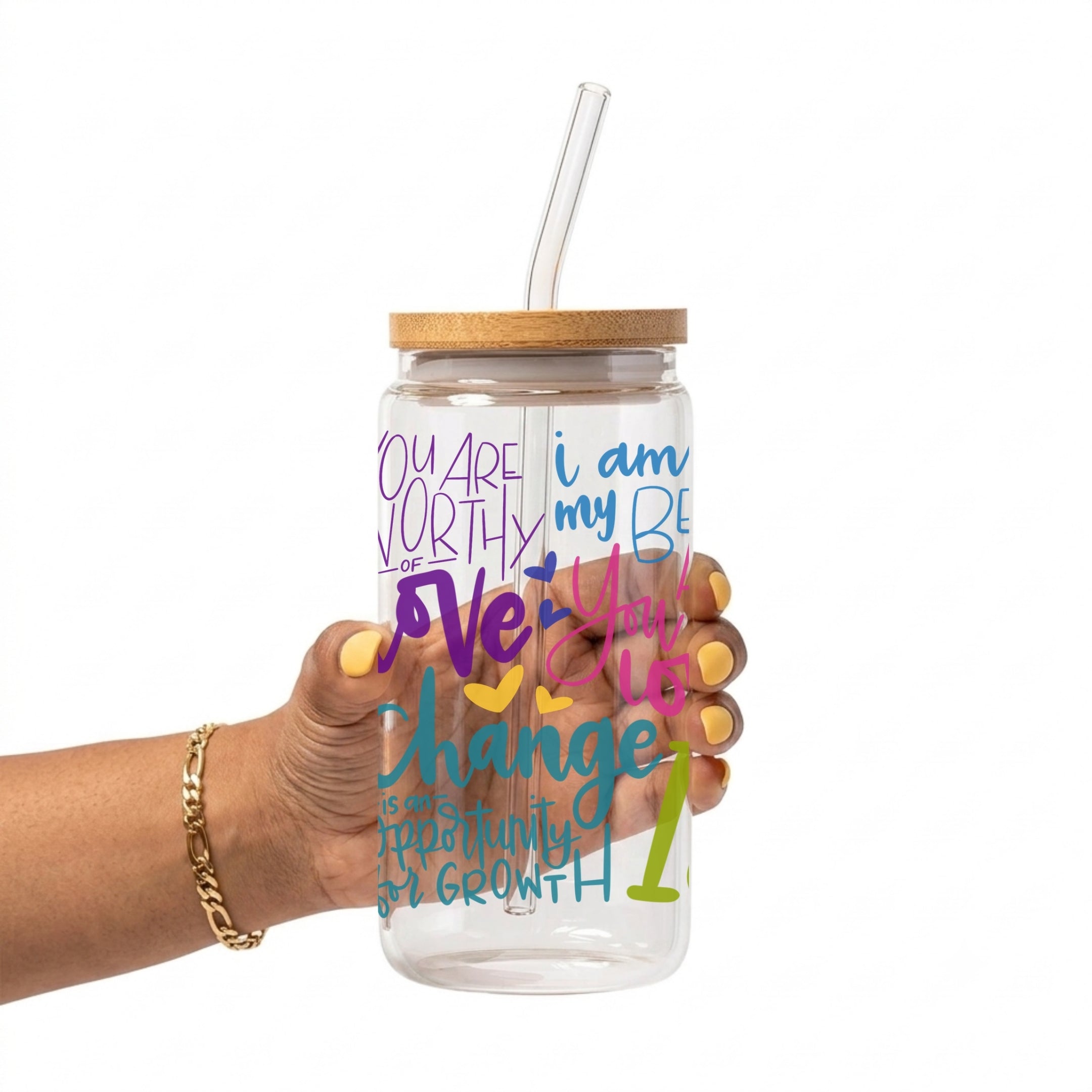 A hand holding a clear glass water bottle with a bamboo lid and clear straw. The bottle features colorful text in purple, blue, pink, yellow, and green.
