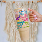 Nik Austin's hand holding a clear mug with colorful text design against a textured wall.
