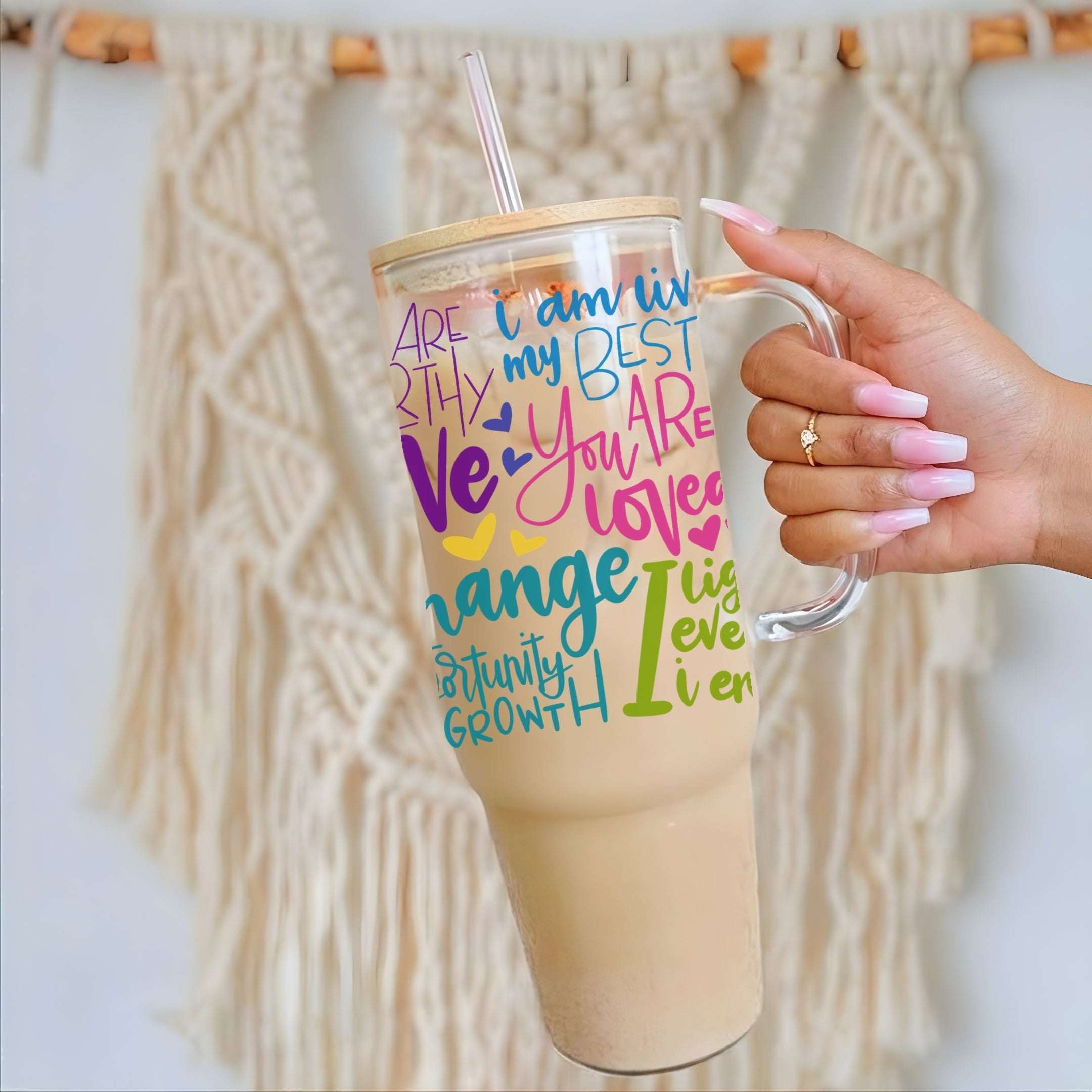 Nik Austin's hand holding a clear mug with colorful text design against a textured wall.