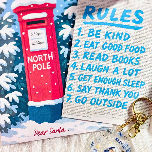 Christmas-themed card with a red mailbox, a keychain, and a 'Rules' list on a wooden surface.