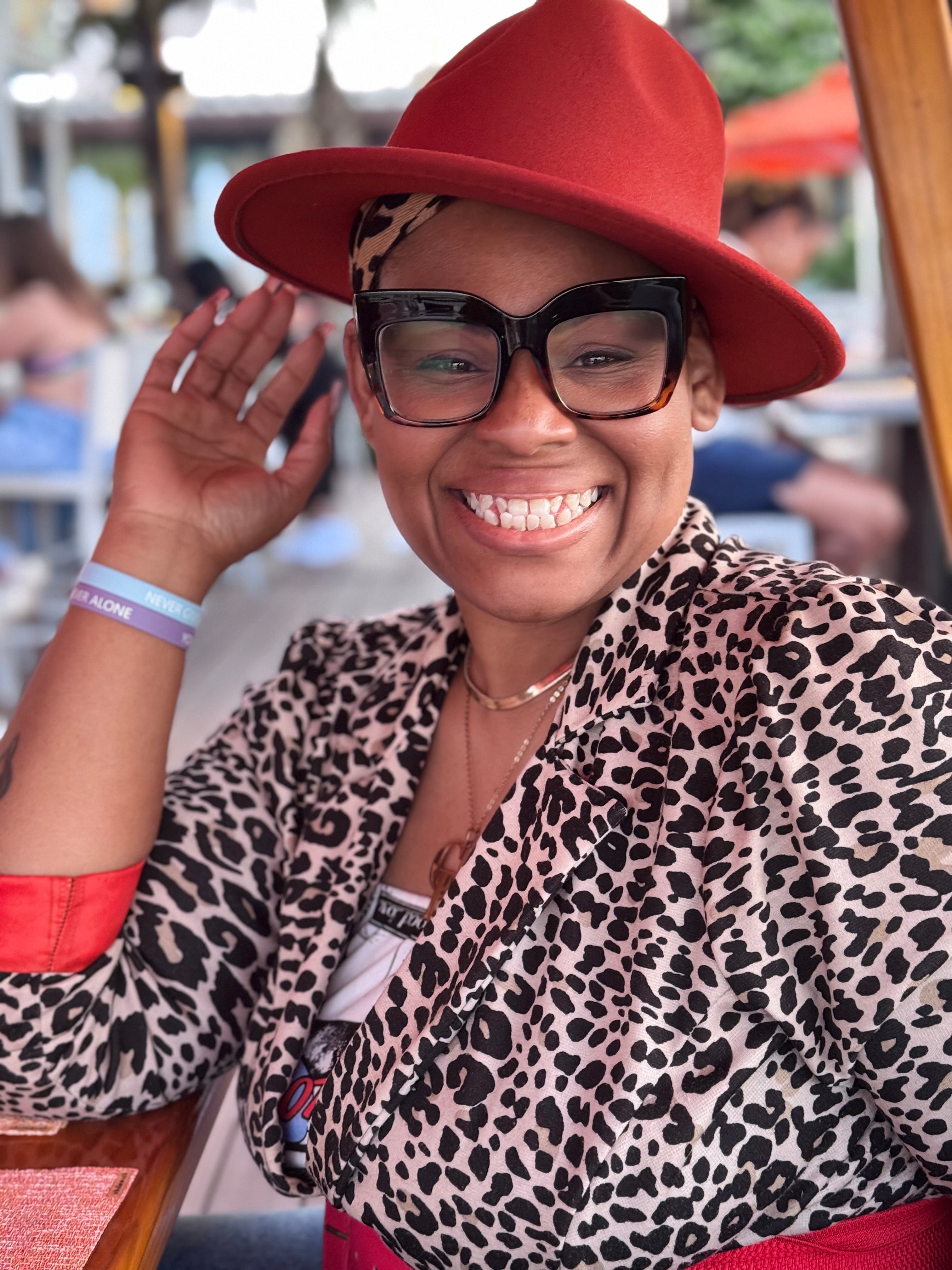 nik austin wearing a red hat and leopard print outfit, smiling outdoors.