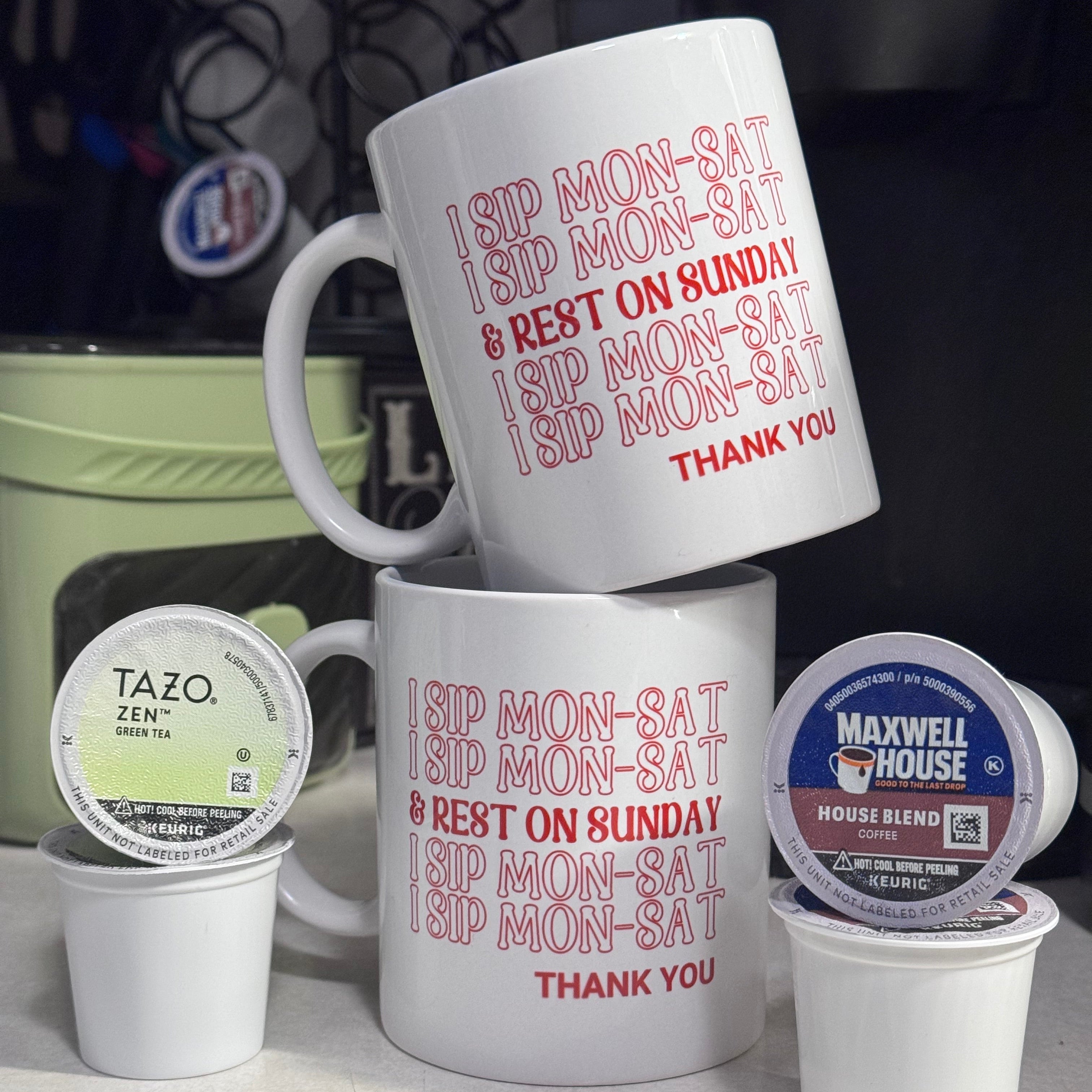 Two white mugs with I Sip Mon-Sat and three coffee pods on a light surface.