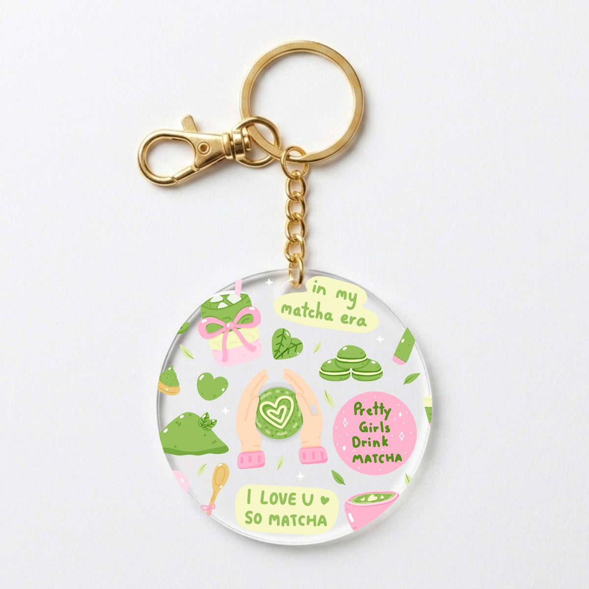 A round acrylic keychain charm featuring a cute matcha-themed illustration with green tea leaves, pink matcha sweets, and the text 'in my matcha era' and 'I LOVE U SO MATCHA'. The charm is attached to a gold-tone metal chain and clasp, shown on a clean white background.