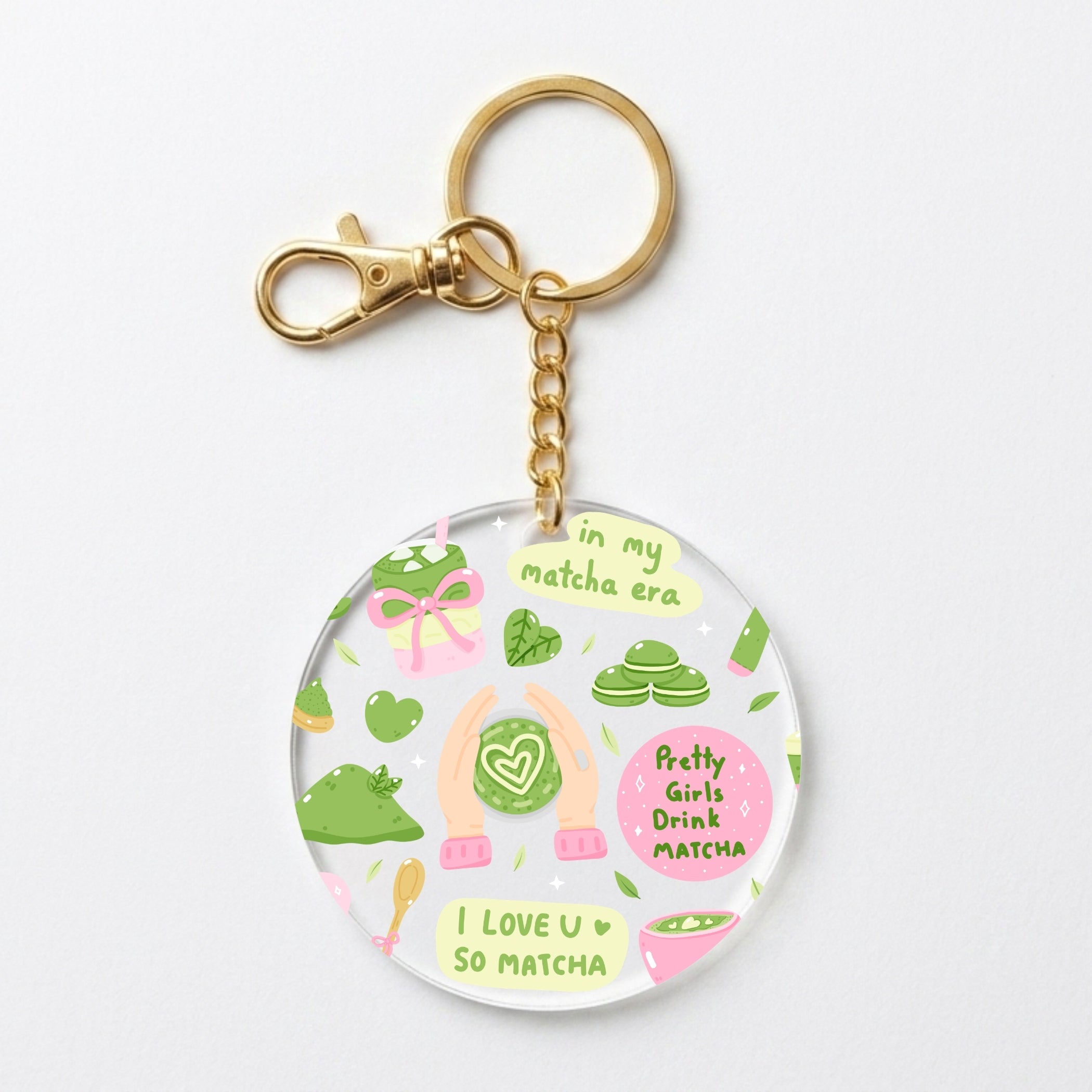 A round acrylic keychain charm featuring a cute matcha-themed illustration with green tea leaves, pink matcha sweets, and the text 'in my matcha era' and 'I LOVE U SO MATCHA'. The charm is attached to a gold-tone metal chain and clasp, shown on a clean white background.