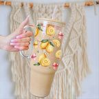 Glass tumbler with lemon design held by a hand against a textured wall.