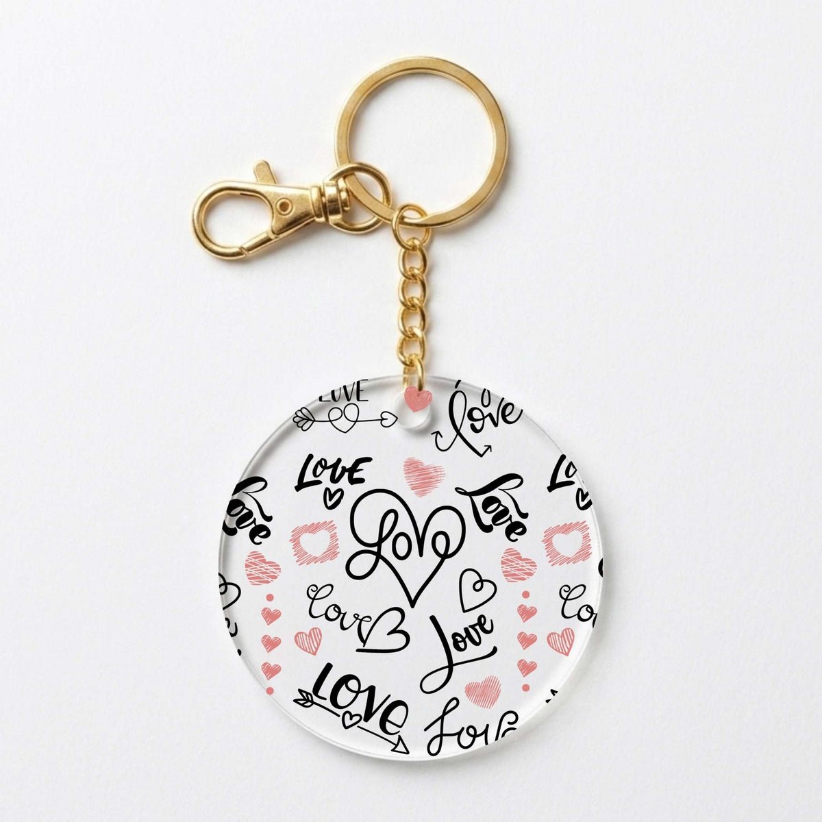 A round acrylic keychain charm featuring a white background with black and pink hand-drawn hearts, hearts, and the word 'Love' in various script styles, attached to a gold-tone split ring and clasp.