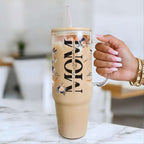 Nik's hand holding a clear tumbler with floral design and 'MOM' text, filled with a beige beverage.