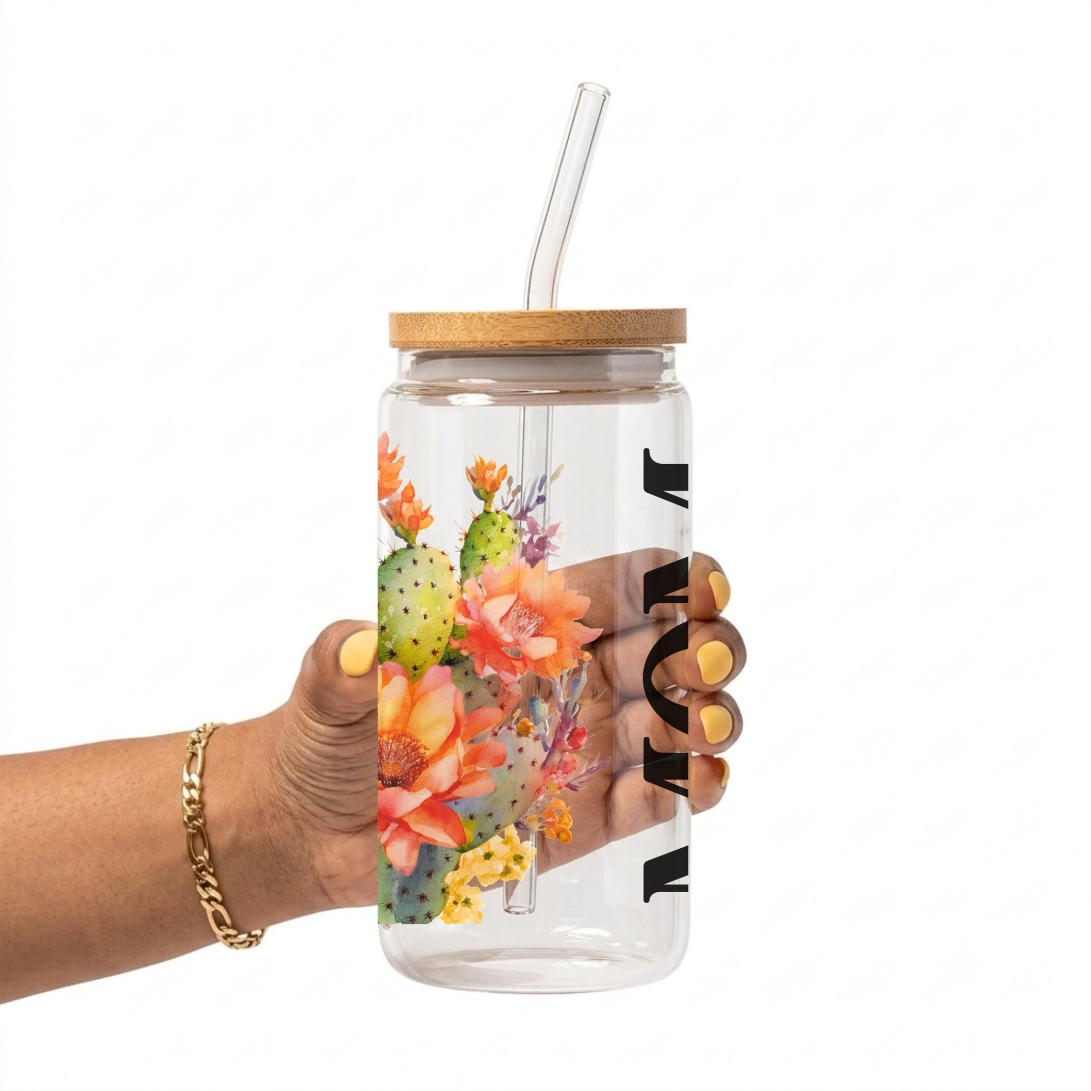 A hand holding a clear plastic tumbler with a bamboo lid and clear glass straw, decorated with a colorful desert floral and cactus print and black lettering, on a white background.