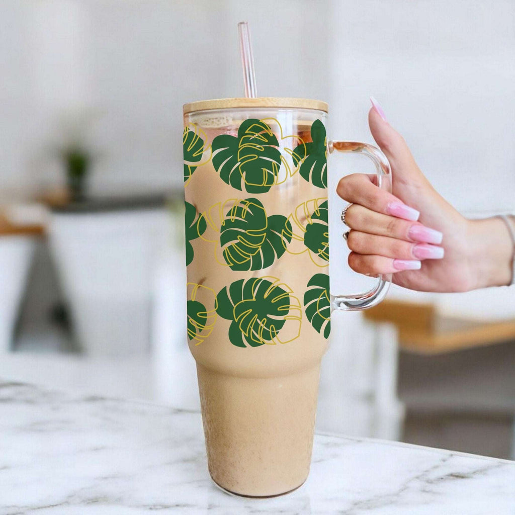 Tumbler with green leaf pattern held by a hand on a marble surface