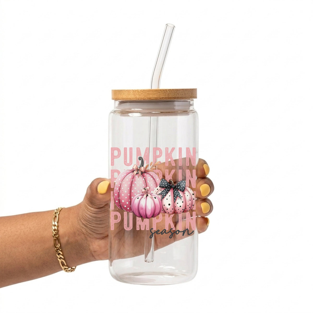 A hand holding a clear glass 16oz tumbler with a bamboo lid and clear straw. The tumbler features a graphic of pink watercolor pumpkins with a black bow and the text 'PUMPKIN season' in pink and black script.
