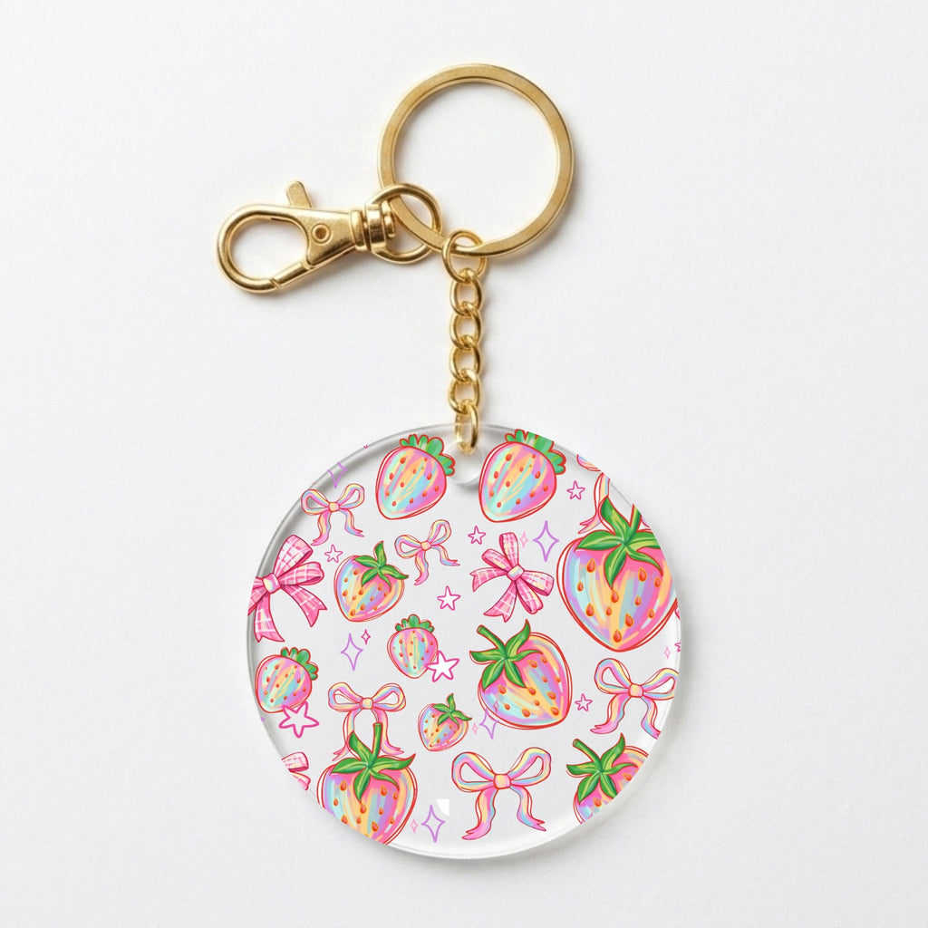 A round acrylic keychain charm featuring a colorful watercolor strawberry and bow pattern, attached to a gold-tone metal split ring and clasp on a plain white background.