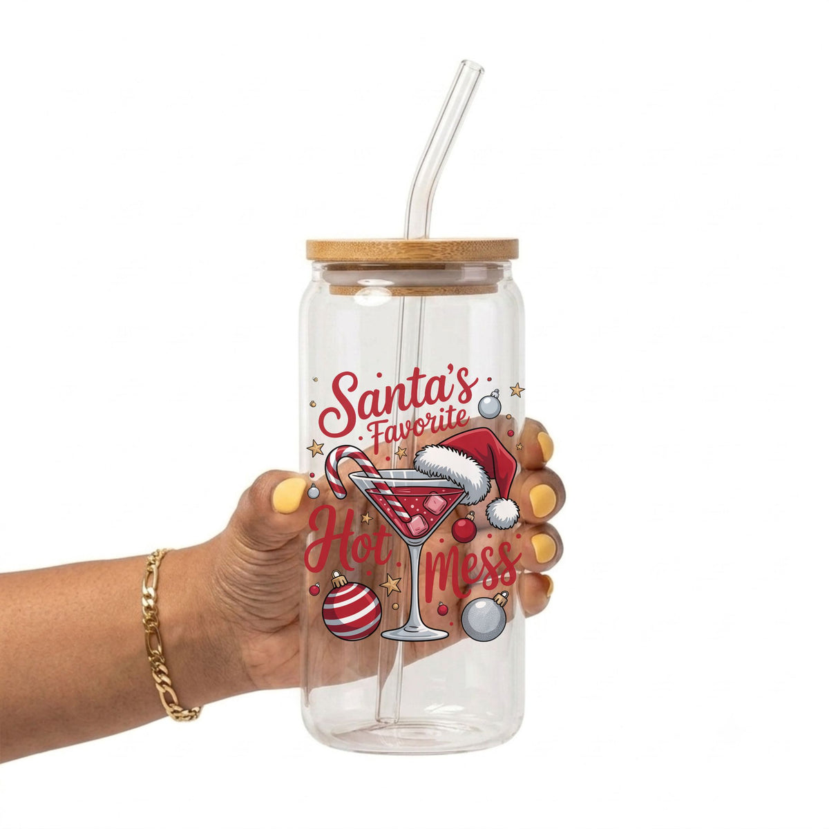 A hand holding a clear glass tumbler with a bamboo lid and clear straw, decorated with a Christmas graphic that reads 'Santa's Favorite Hot Mess' with a martini glass, Santa hat, and ornaments on a white background.