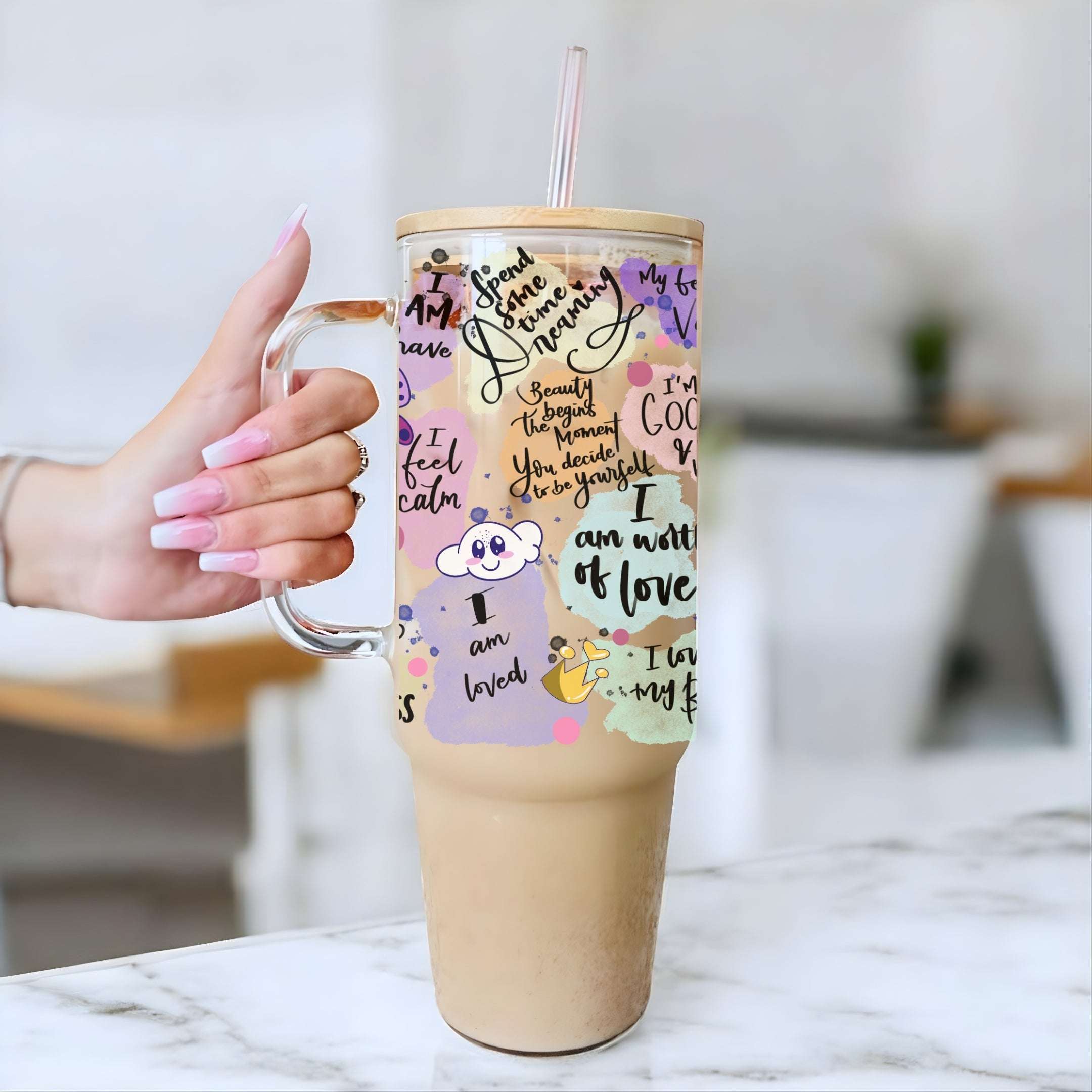 Person holding a tumbler with motivational quotes and cartoon characters on a blurred indoor background