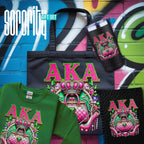 A Sorority gift set featuring multiple apparel and accessories with a matching graphic design. The set includes a black tote bag, a green t-shirt, a black tumbler, and a black spiral notebook, all decorated with a pink and green crown-and-lock graphic and the letters 'AKA'.