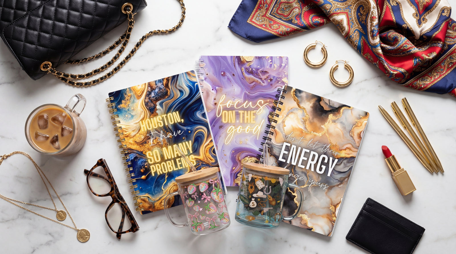 Three self-love journals with motivational text on a marble surface with accessories and 17oz glass mugs.
