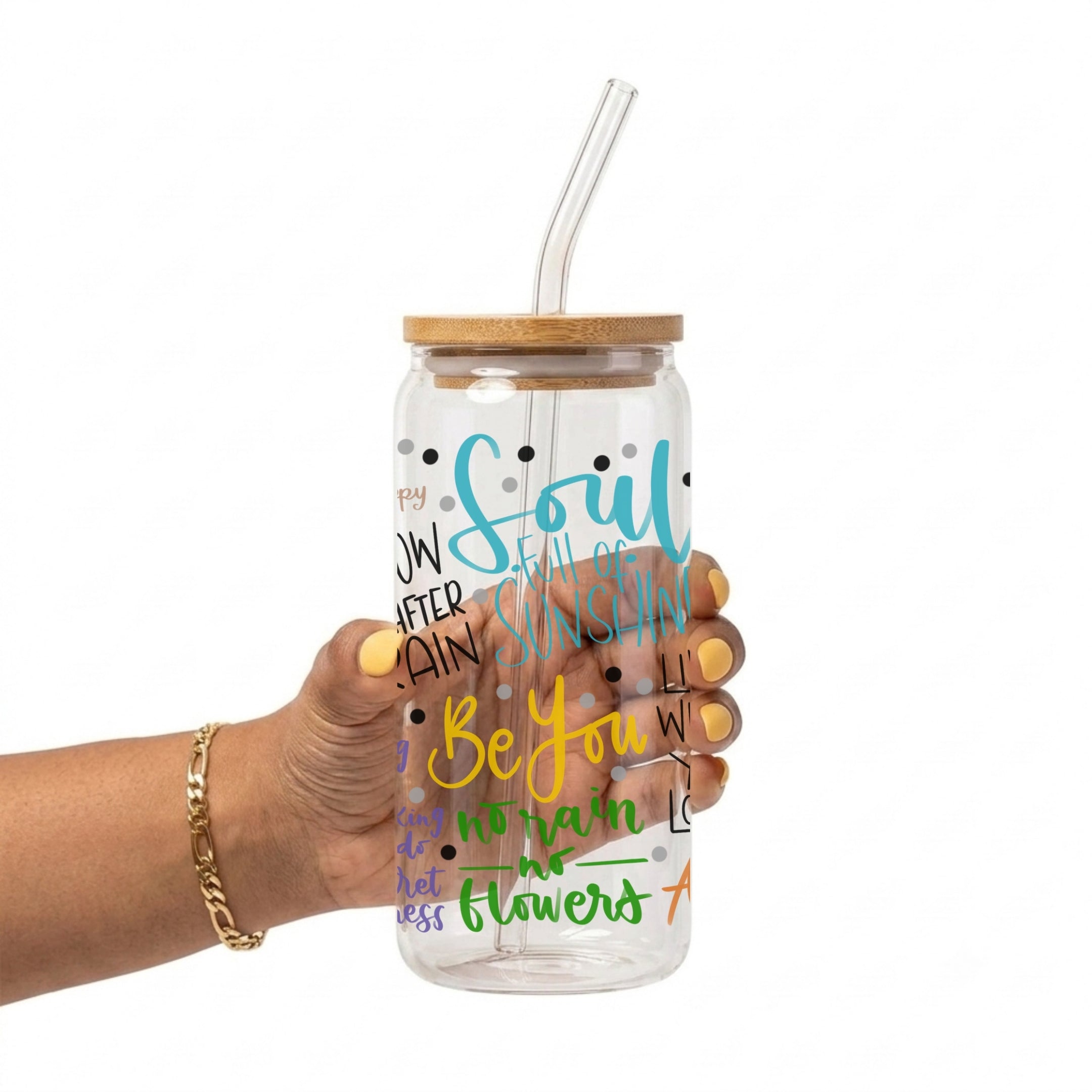 A hand holding a clear plastic water bottle with a bamboo lid and clear glass straw. The bottle features colorful inspirational text including 'Soul Full of Sunshine', 'Be You', and 'No Rain No Flowers'.