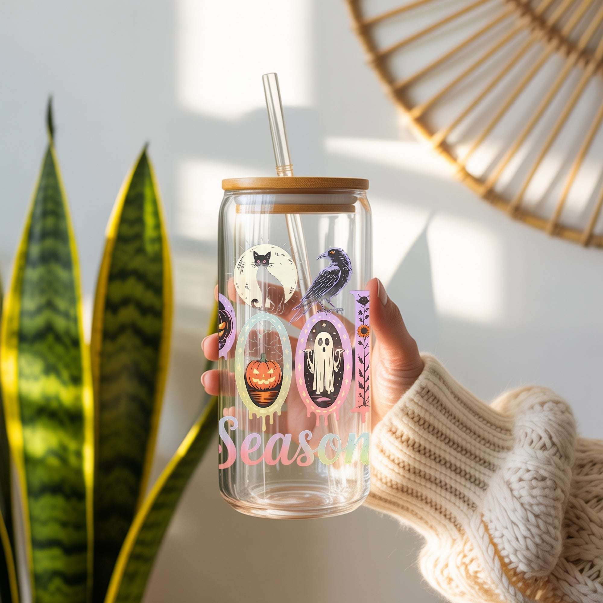 Clear tumbler with Halloween-themed design and straw, held by a person wearing a beige sweater.