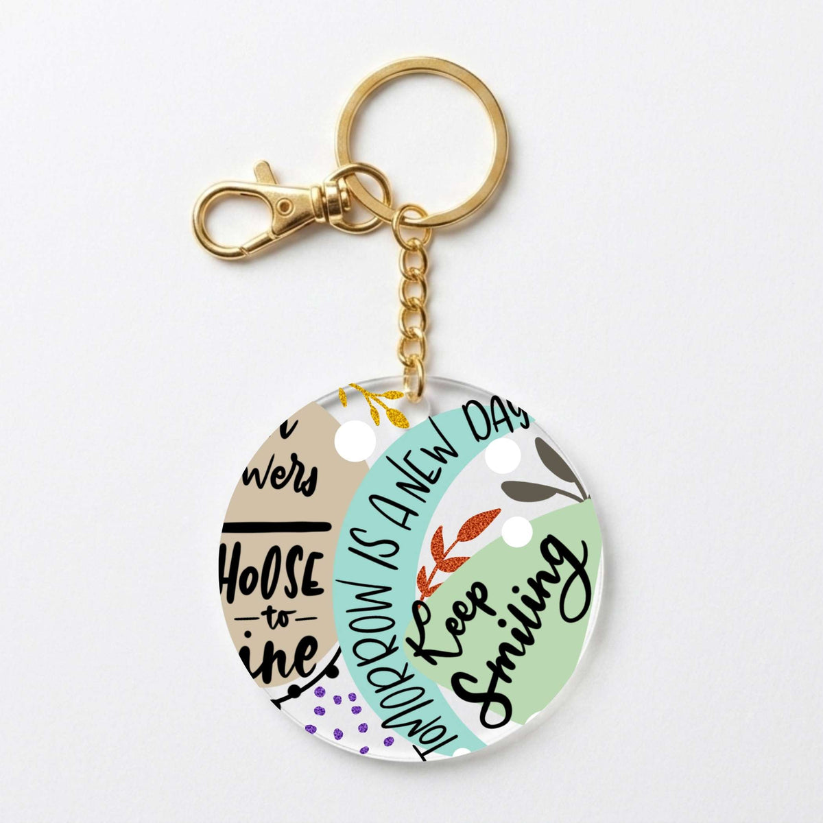 A round acrylic keychain charm with a gold-tone clasp and chain, featuring a pastel multicolor design with text including 'Choose to shine' and 'Tomorrow is a new day' on a light gray background.