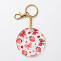 A round acrylic keychain charm featuring a pattern of red strawberries, pink bows, and butterfly bows on a white background, attached to a gold-tone split ring and lobster clasp.
