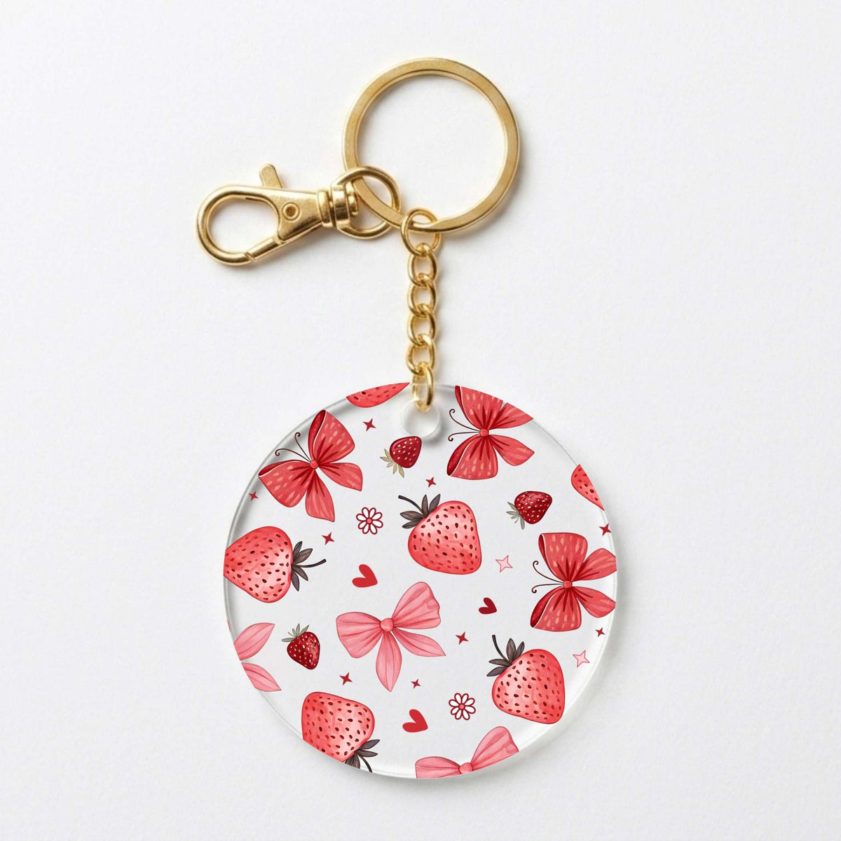 A round acrylic keychain charm featuring a pattern of red strawberries, pink bows, and butterfly bows on a white background, attached to a gold-tone split ring and lobster clasp.