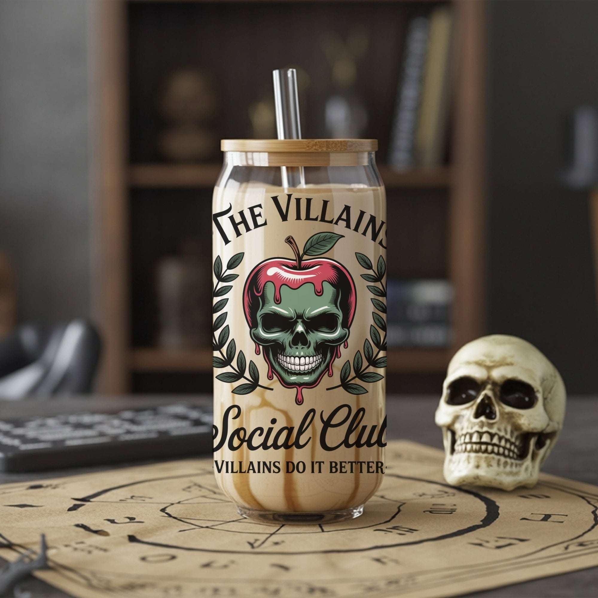 Glass tumbler with skull design and text on a table with a skull and bookshelf in the background
