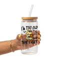 A hand holding a clear glass tumbler with a bamboo lid and clear straw. The tumbler features a cartoon graphic of a ghost wearing sunglasses and holding a mug, with the text 'I'M TOO OLD FOR THIS SHEET' in black.