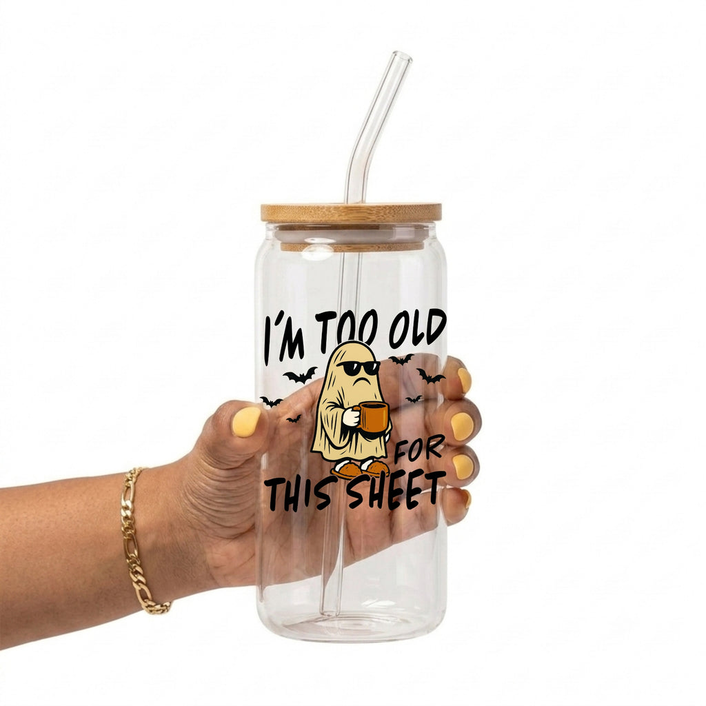 A hand holding a clear glass tumbler with a bamboo lid and clear straw, featuring a cartoon ghost graphic and the text 'I'M TOO OLD FOR THIS SHEET' on a white background.