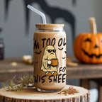 Glass tumbler with Halloween-themed design and text on a wooden surface with pumpkins in the background