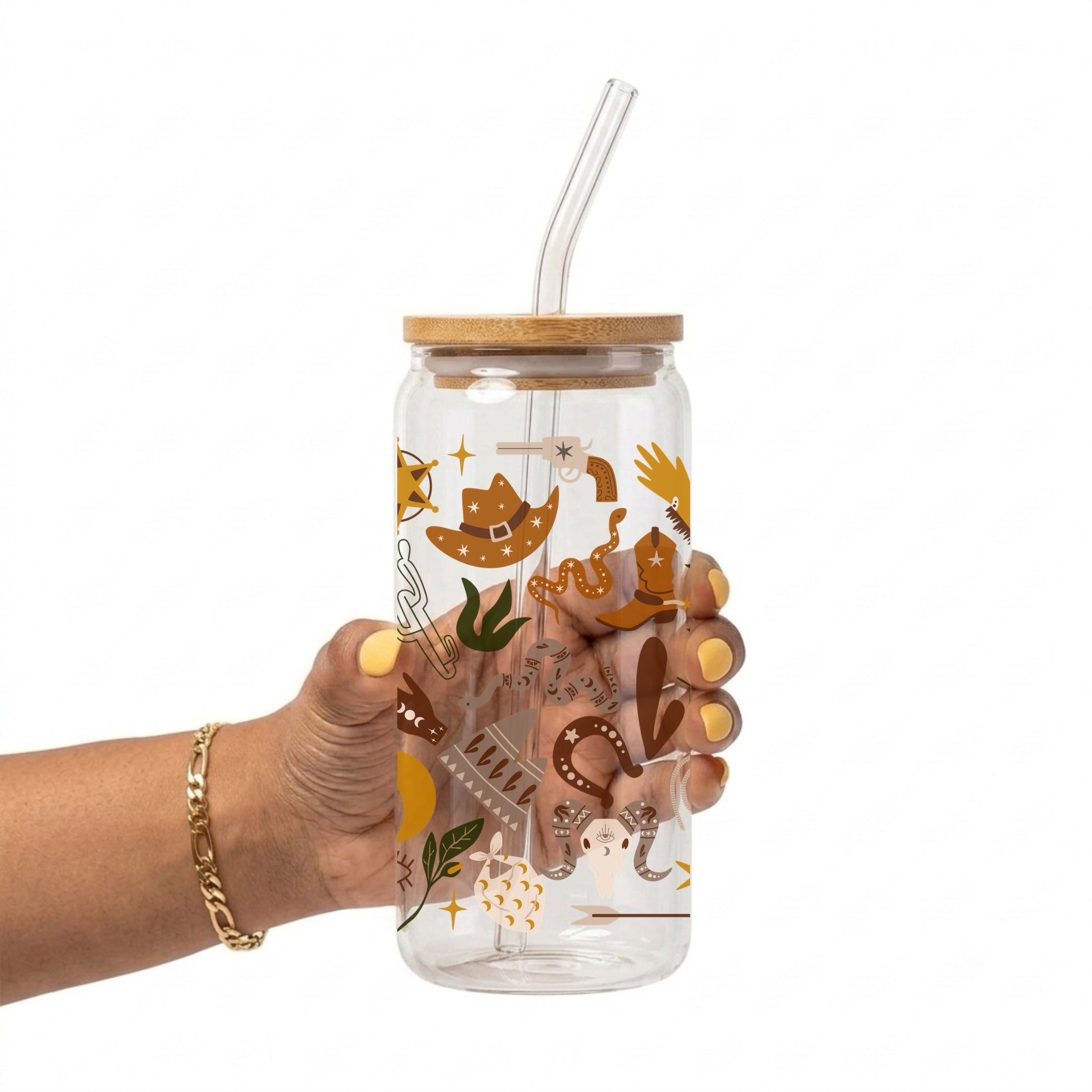 A hand holding a clear glass tumbler with a bamboo lid and clear glass straw, decorated with a rustic western-themed pattern of brown cowboy hats, boots, horseshoes, and gold stars.