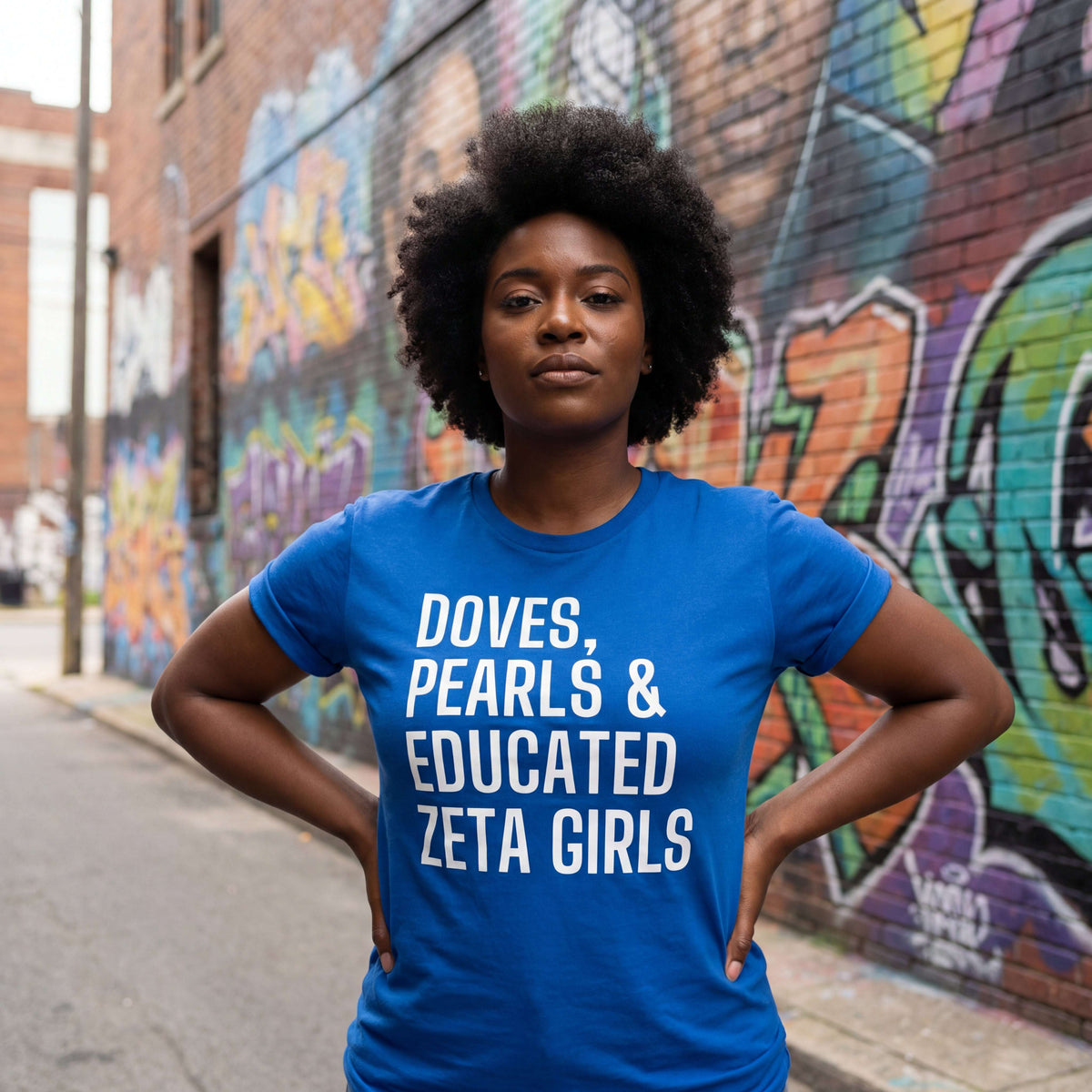 A Zeta wearing a blue Doves, Pearls, & Educated Zeta Girls t-shirt in an urban setting with graffiti.