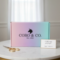 Gradient box with 'CORO & CO.' branding on a marble surface with a card and scissors.