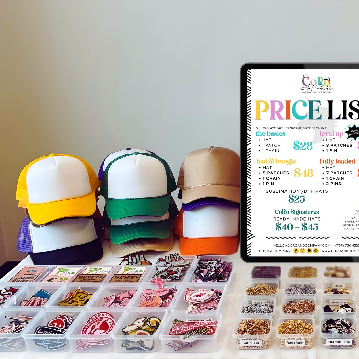 Colorful trucker caps and accessories with an iPad displaying a price list on a table.