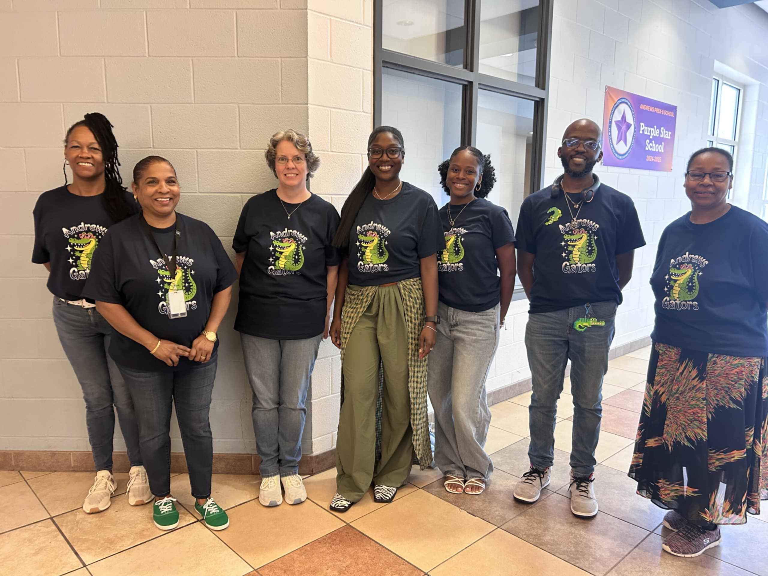 Group of people wearing matching navy blue t-shirts with a green graphic in a hallway.