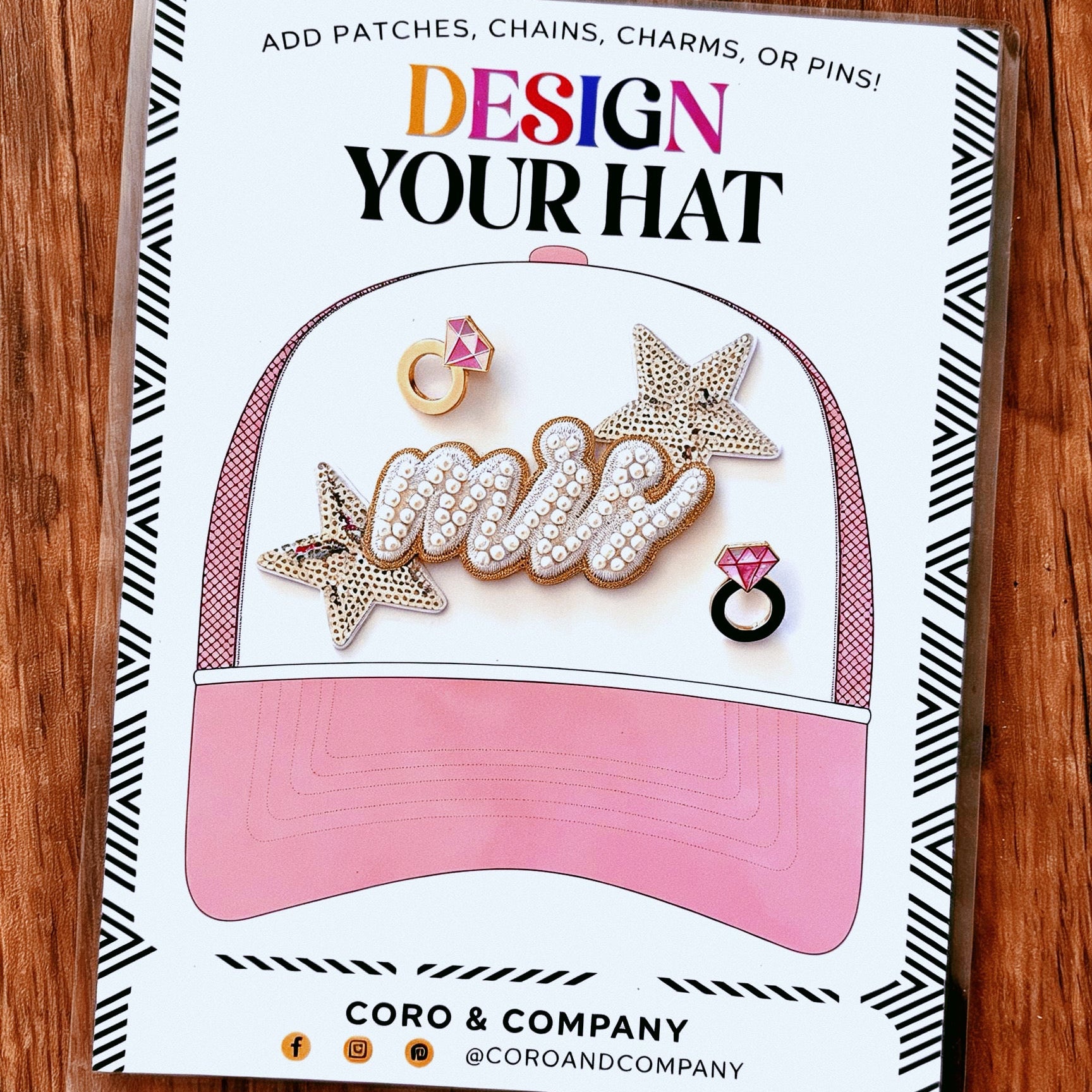 Cardboard sheet with 'Design Your Hat' text and pink cap illustration on a wooden surface